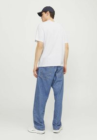 Hvid bomulds-t-shirt, afslappet pasform, parret med blå løse denimjeans og hvide sneakers. Personen har en mørk kasket på.
