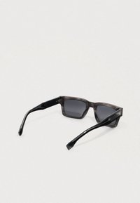 Óculos de sol quadrados com armação cinza fumada translúcida e hastes pretas sólidas. Lentes escuras, ferragens minimalistas e design elegante.