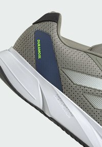 Scarpa da atletica grigia con tomaia in mesh, intersuola bianca e suola in gomma scura. Presenta la scritta "DURAMOSL" e dettagli testurizzati per una migliore aderenza.