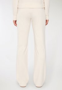 Osoba ubrana w luźne, kremowe spodnie dresowe i pasującą bluzę, pokazana od tyłu na tle białego tła.