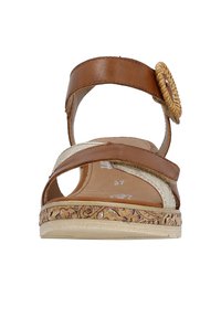 Sandale en cuir marron avec une sangle ajustable, des accents dorés et un détail tissé décoratif. Présente une semelle extérieure texturée avec un motif floral.