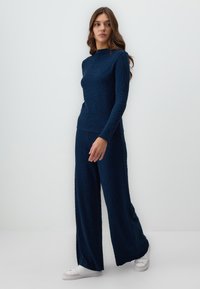 Navy gewatteerde lounge-set met een lange mouw top met een hoge halslijn en brede broekspijpen, gecombineerd met witte sneakers.