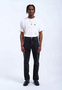 Camiseta blanca de algodón con mangas cortas, combinada con jeans de mezclilla negros. Zapatos negros completan el conjunto. Joyería sencilla realza el look.