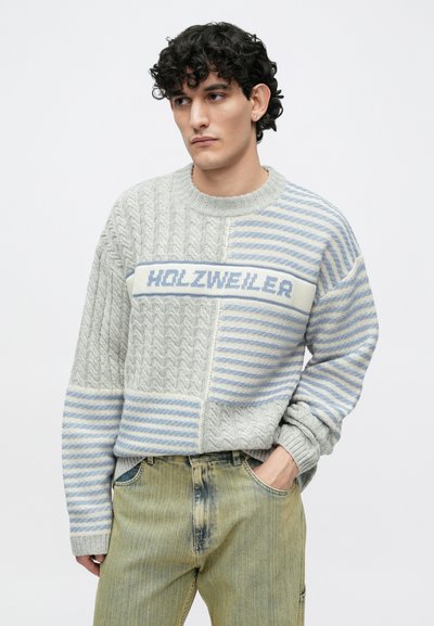 Világosszürke kötött pulóver, fonott és csíkos mintákkal. Középen kék logószalaggal. Laza szabás, bordázott mandzsettákkal.