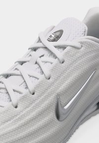 Κοντινό πλάνο ενός λευκού αθλητικού παπουτσιού Nike με πλέγμα υφή, λευκά κορδόνια και ασημί λογότυπο Nike στο πλάι.