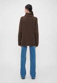 Brauner Strickpullover mit hohem Kragen, entspannter Passform und geripptem Saum, kombiniert mit hellblauen weitem Jeans. Glatte Textur und vielseitiges Design.