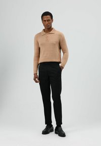 Beige gebreide polotrui met een kraag en een patte met drie knopen, gecombineerd met zwarte op maat gemaakte broek en zwarte loafers.