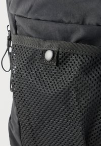 Μαύρο σακίδιο πλάτης με δίχτυνο τσαντάκι που έχει κυκλικά σχέδια, ασφαλισμένο με πλαστικό κούμπωμα και ανθεκτική υφασμάτινη κατασκευή.