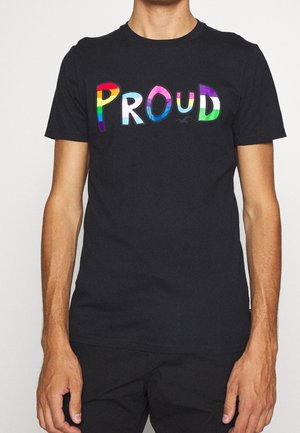 T-shirt noir avec le mot « PROUD » en grandes lettres colorées, chacune stylisée avec différents motifs de drapeaux de la fierté LGBTQ+.
