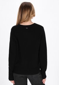 Maglione nero a maglia con scollatura tonda e maniche lunghe, con orlo a costine e un piccolo etichetta logo sul retro. Texture morbida.