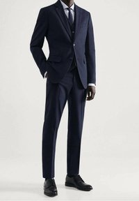 Marineblauw pak met een op maat gemaakt blazer met notch revers en een drieknoopsluiting, gecombineerd met een slim-fit broek en zwarte klassiekerschoenen.