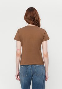 Brown cotton t-shirt with short sleeves, a round neckline, and a slightly fitted shape, paired with blue denim jeans.