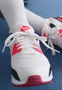 Sapatilhas brancas da Nike com acentos vermelhos, camadas texturizadas e detalhes em preto. Possui atacadores planos e uma sola almofadada em vermelho.