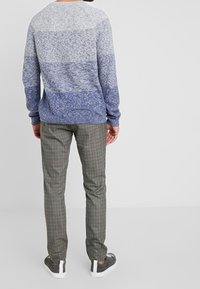 Blauer Pullover mit Farbverlauf, langen Ärmeln und strukturiertem Strick, kombiniert mit grauen karrierten Hosen und grauen Sneakers mit weißen Akzenten.