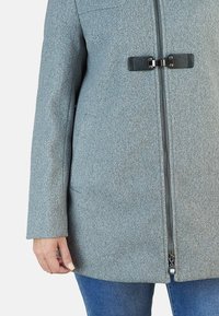 Abrigo de mezcla de lana gris con cremallera frontal, cierre de toggle y bolsillos laterales, con una textura suave y una silueta entallada.
