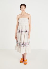 Strapless, beige maxi-jurk met verticale strepen, gerimpelde buste, kleurrijke bloemenborduursel en een gerimpelde zoom. Gemaakt met oranje platform sandalen.