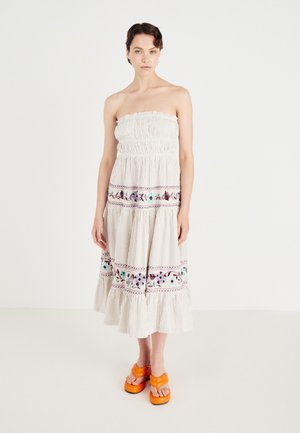 Strapless, beige maxi-jurk met verticale strepen, gerimpelde buste, kleurrijke bloemenborduursel en een gerimpelde zoom. Gemaakt met oranje platform sandalen.