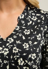 Tessuto nero con motivo floreale e fiori crema; design a V; texture liscia; dettagli di cucitura prominenti vicino al collo.