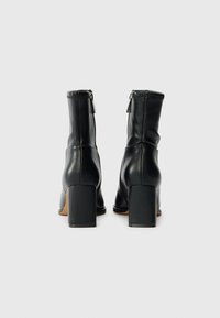 Black leather ankle boots with a fitted design, square high heels, and back zippers; smooth texture and clean lines.