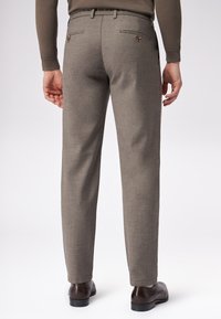 Brązowe, strukturalne spodnie o prostym kroju, z tylnymi kieszeniami zapinanymi na guziki, noszone z ciemnymi skórzanymi butami.