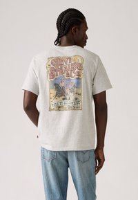 Camiseta cinza de manga curta com um gráfico vintage colorido da Levi Strauss & Co. nas costas, com um clássico decote redondo e um ajuste descontraído.