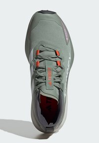 Chaussure d'extérieur verte avec une tige texturée, des panneaux en maille, des accents orange et une semelle en caoutchouc grise. Elle dispose de lacets et de marquage sur les côtés.