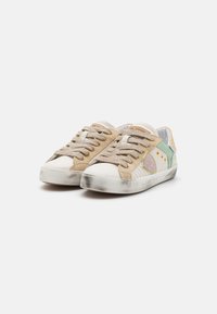 Beige suede sneakers with white rubber soles, featuring textured laces, green and purple accents, and subtle scuffing on the toe.