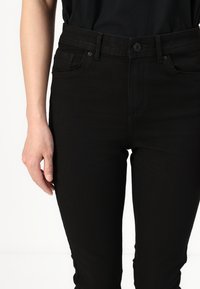 Black denim jeans feature a fitted design with a smooth texture, five-pocket styling, and a button closure at the waist.