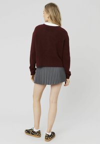 Pull bourgogne, jupe plissée grise, et baskets à imprimé léopard noir avec une semelle crème. Texture douce, coupe décontractée et design superposé.