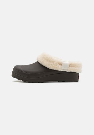 Black clog with a fluffy cream-colored lining and white strap. Textured sole for grip; smooth exterior. Casual, slip-on design.
