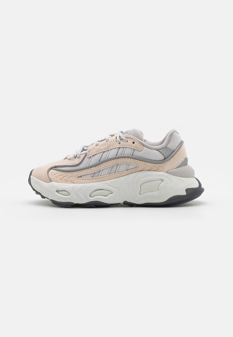 Sneaker mit einem strukturierten, hellbeigen Obermaterial, grauen Akzenten und einer klobigen weißen Sohle mit Wellenmuster. Verfügt über graue Schnürsenkel und Ösen.