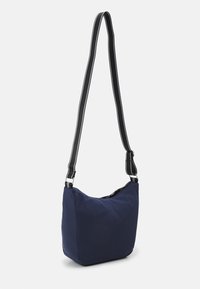 Navy blue fabric shoulder bag with a curved shape, adjustable black strap with white accents, and a top zip closure. Minimalist design.