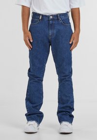 Denim farkut sinisellä pesulla, suora malli, viisi taskua, etunappi kiinnitys ja hienovaraiset ompelutiedot. Yhdistetty valkoisten lenkkareiden kanssa.