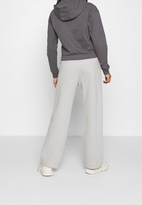 Felpa grigia corta con cappuccio, abbinata a pantaloni sportivi larghi di un grigio chiaro, che presentano una texture semplice e morbida. Sneakers bianche completano il look.