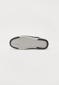 Talpa de adidasi negri cu un model texturat pentru prindere, având o talpă intermediară din cauciuc alb și un logo embosat. Margini netede și design cu vârf rotunjit.