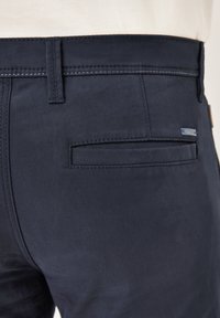 Marinefarbene Stoffhosen mit einer flachen Gesäßtasche, kontrastierenden Nähten und einem kleinen Markenetikett am Bund. Glatte Textur.