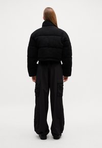 Svart kort pufferjakke med høy krage og teksturert stoff, kombinert med løse svarte cargo-bukser med sidelommer.