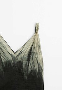 Robe sans manches à col en V avec fines bretelles, motif tie-dye vert et noir, posée à plat sur un fond blanc.