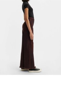 Vaqueros anchos de color rojo oscuro con dobladillo deshilachado, diseño de tiro alto y detalles de botones dorados, combinados con zapatillas negras y una camiseta ajustada negra.