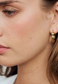 Guld oval hoopörhängen med en slät, reflekterande yta. Har en staplad pärldesign som visar upp en polerad textur och subtil glans.