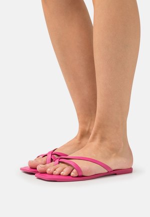 Platta sandaler i livlig rosa med ett korsat remdesign, tillverkade av ett mjukt material. Öppen tå med en minimalistisk stil och platt sula.