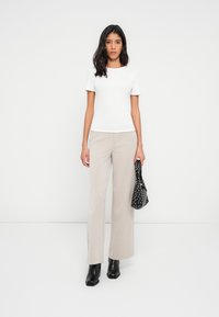 White short-sleeve fitted top, beige wide-leg trousers, and black ankle boots. Holding a black polka dot bag. Simple, clean design.
