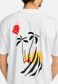 Witte t-shirt met een kleurrafische afbeelding van palmbomen, een zon en abstracte vormen in rood, geel en zwart op de achterkant.