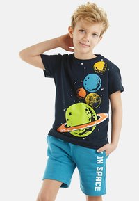 Camiseta navy con gráficos coloridos de planetas y estrellas, combinada con pantalones cortos verde azulado que tienen impreso "EN EL ESPACIO" en blanco.