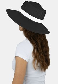 Schwarzer, breitkrempiger Hut aus geflochtenem Material, mit einem weißen Akzentband. Das Design ist strukturiert und texturiert und bietet Sonnenschutz.