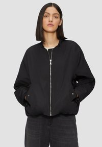 Blouson noir en coton avec fermeture éclair à l'avant, col montant et poches latérales. Fabriqué dans un tissu lisse avec une coupe légèrement oversize.