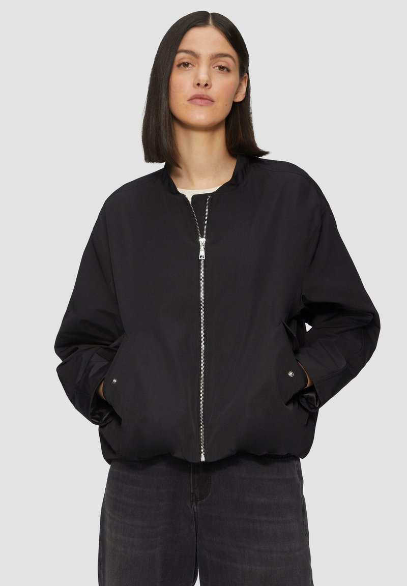 Blouson noir en coton avec fermeture éclair à l'avant, col montant et poches latérales. Fabriqué dans un tissu lisse avec une coupe légèrement oversize.