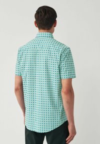 Kurzarm-Hemd mit Knopfleiste in Teal mit einem geometrischen weißen Muster. Glatte Stoffqualität, klassischer Kragen und abgerundetem Saum.
