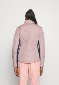 Jasnoróżowa, ocieplana kurtka z wzorem w kształcie szewronu i wysokim kołnierzem. Ciemnoniebieskie boczne panele. Na dole znajduje się logo.