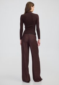 Brauner gerippter Rollkragenpullover mit langen Ärmeln, kombiniert mit weit geschnittenen Karohosen mit einem rot-braunen Checkmuster und einem Reißverschluss.